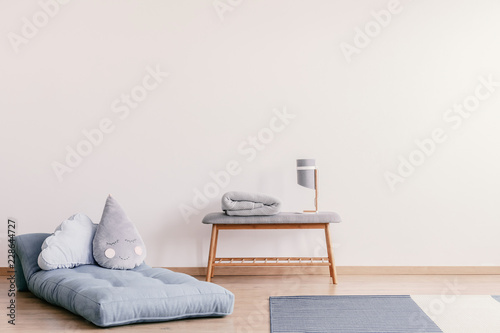 Futon with cute pillows on the floor of stylish baby room interior with copy space on the empty white wall