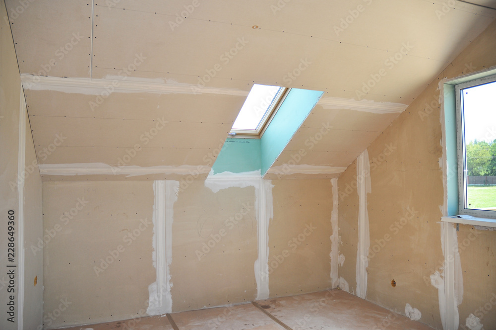 Drywall construction in unfinished house attic with skylight. Drywall