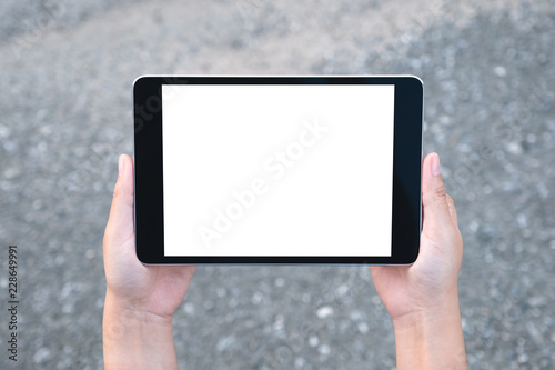 Top view mockup image of hands holding black tablet pc with blank white screen with street background