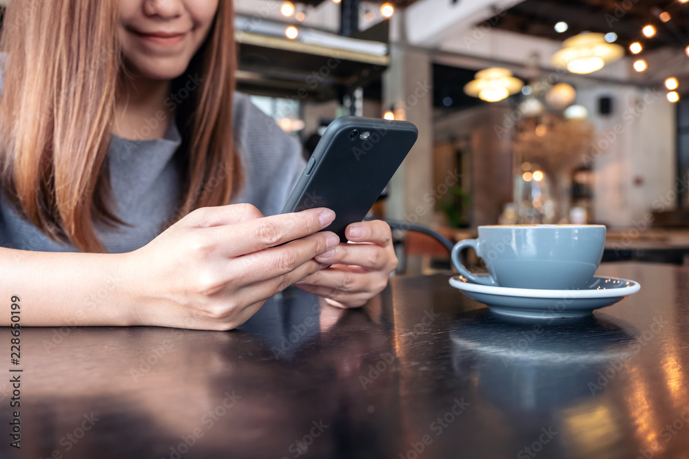 Closeup image of a woman holding and using a smart phone with coffee cup on table Closeup image of a woman holding and using a smart phone with coffee cup on table