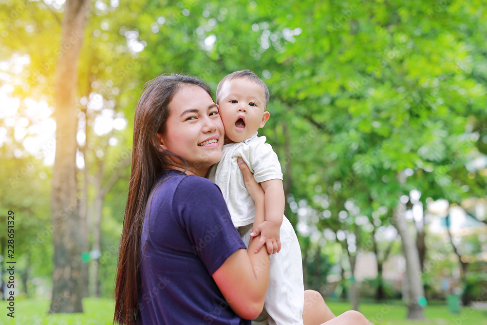 Asian mother carrying her infant baby boy in the summer garden. Asian mother carrying her infant baby boy in the summer garden.