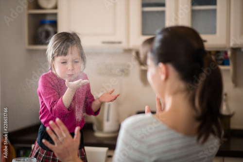 Daughter blowing flour on mother during baking