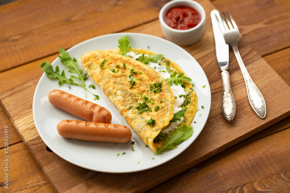 Omelette with herbs, soft cheese, grilled sausages and tomato sauce. Delicious breakfast Omelette with herbs, soft cheese, grilled sausages and tomato sauce. Delicious breakfast