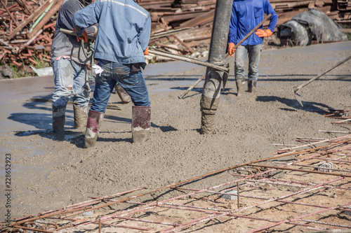 Workers using a wooden spatula for cement after Pouring ready-mixed concrete on steel reinforcement to make the road by mixing mobile the concrete mixer.