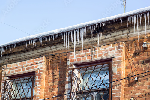 Wintry roof of the house with icicles on blue sky background