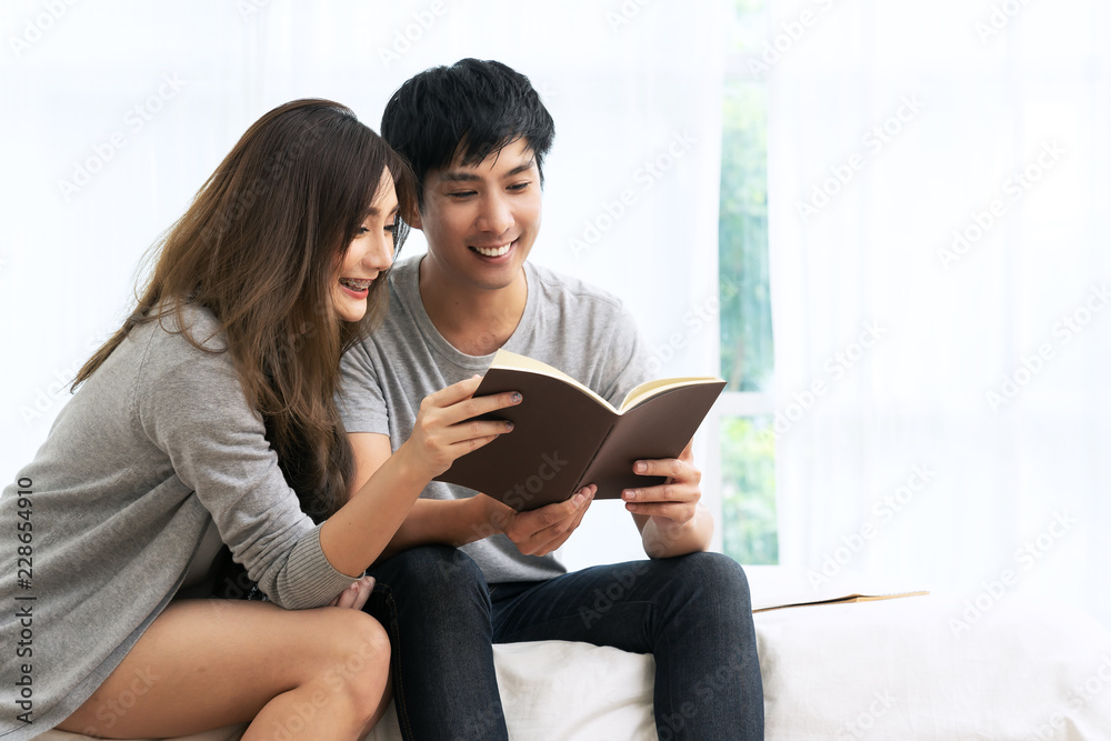 Young asian romantic couple reading book having great time together feeling satisfaction and positive in white bedroom. Close up view of happy lifestyle married couple in leisure family time concept. Young asian romantic couple reading book having great time together feeling satisfaction and positive in white bedroom. Close up view of happy lifestyle married couple in leisure family time concept.