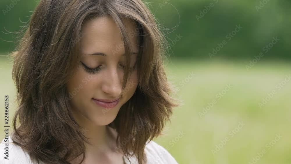 Shy beautiful young woman with brown hair smiles looking down outdoor nature Shy beautiful young woman with brown hair smiles looking down outdoor nature