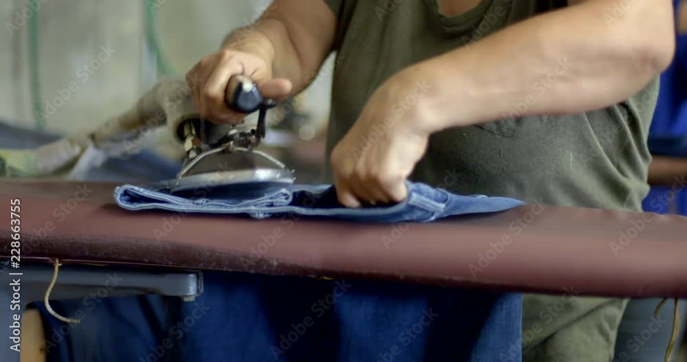 Detail unidentifiable female Hispanic garment industry worker pressing jeans on a steaming ironing board at warehouse in Los Angeles. Slow motion front angle, 4K recorded 60fps Detail unidentifiable female Hispanic garment industry worker pressing jeans on a steaming ironing board at warehouse in Los Angeles. Slow motion front angle, 4K recorded 60fps