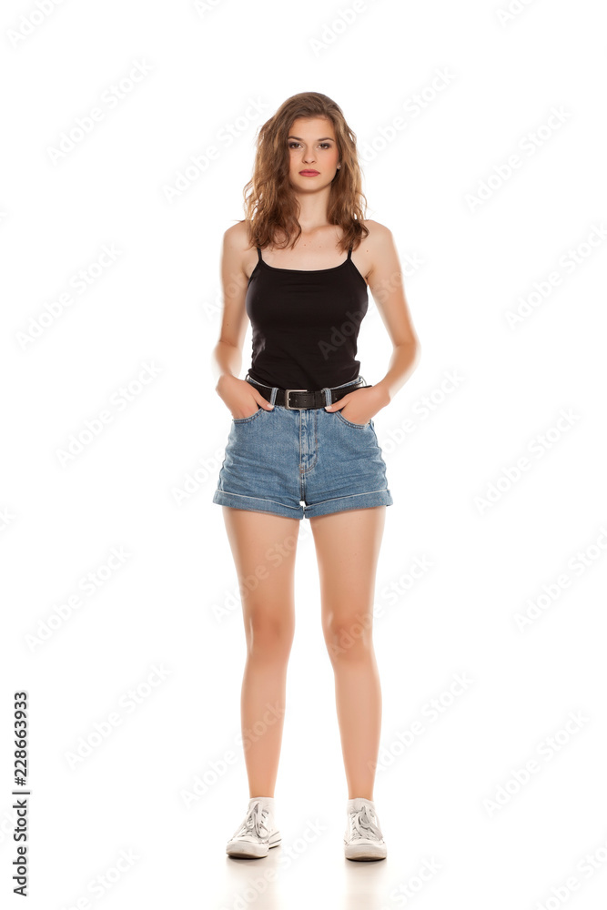 Young pretty woman in short jeans standing on white background Young pretty woman in short jeans standing on white background