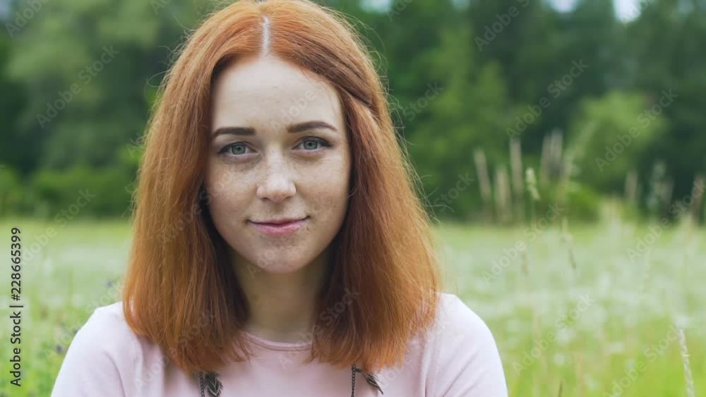 Red haired woman with freckles looks in camera outdoors in field, female smile Red haired woman with freckles looks in camera outdoors in field, female smile
