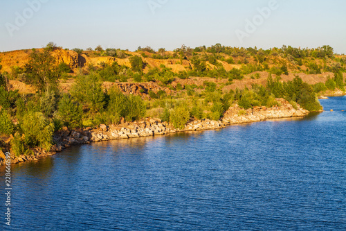 Summer sunset at the pond. Rocky coast with green trees