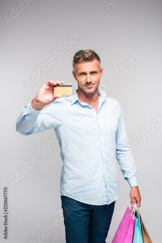 handsome man holding shopping bags and credit card isolated on grey