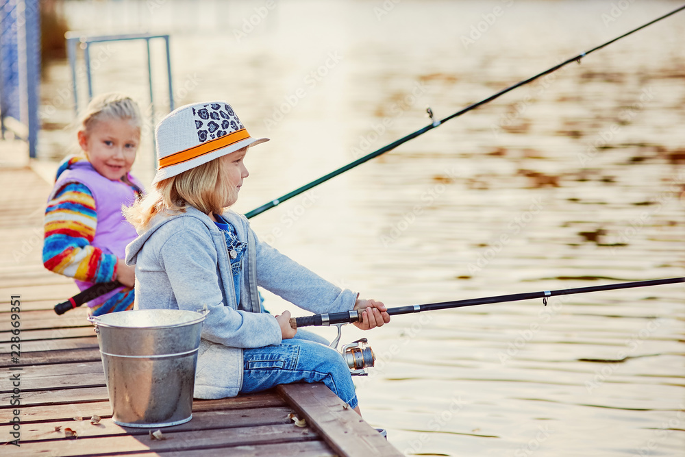 Little girls fishing on the lake, sitting on a wooden pontoon Little girls fishing on the lake, sitting on a wooden pontoon