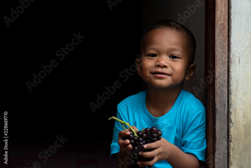 The poor boy is wearing a blue shirt and is eating grapes