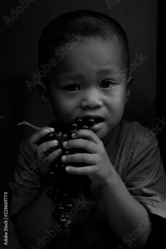 The poor boy is wearing a blue shirt and is eating grapes.black and white picture