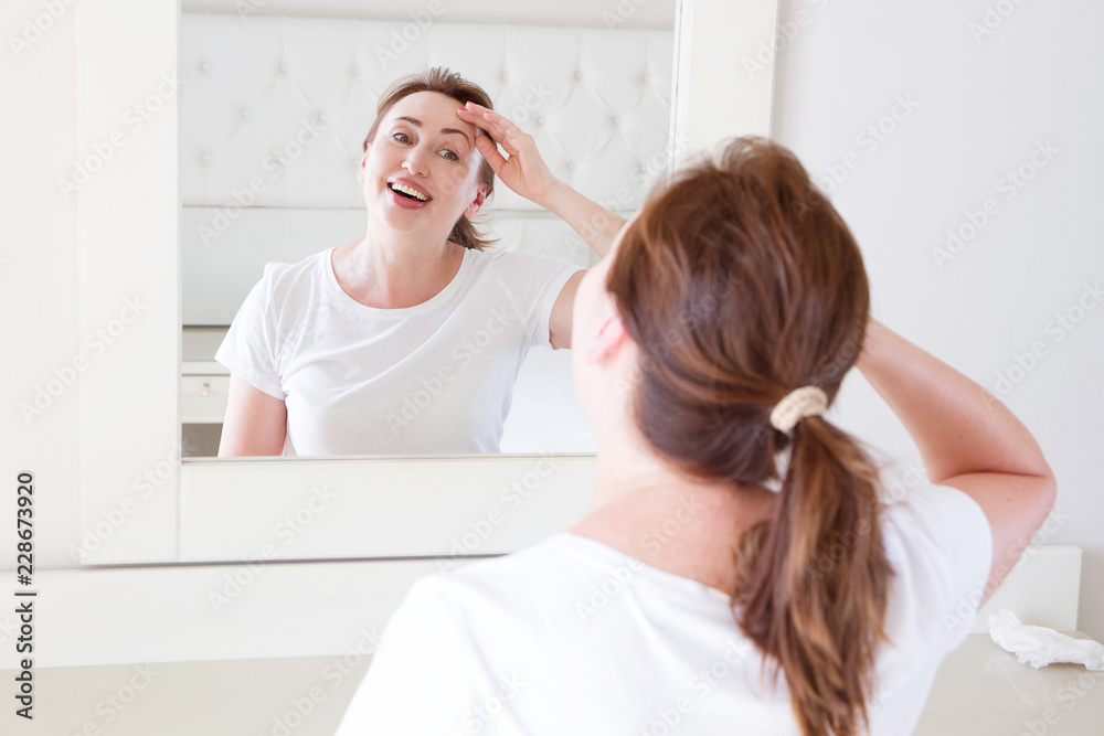 Middle age woman looking in mirror on face wrinkle forehead in bedroom. Wrinkles and anti aging skin care concept. Selective focus Middle age woman looking in mirror on face wrinkle forehead in bedroom. Wrinkles and anti aging skin care concept. Selective focus