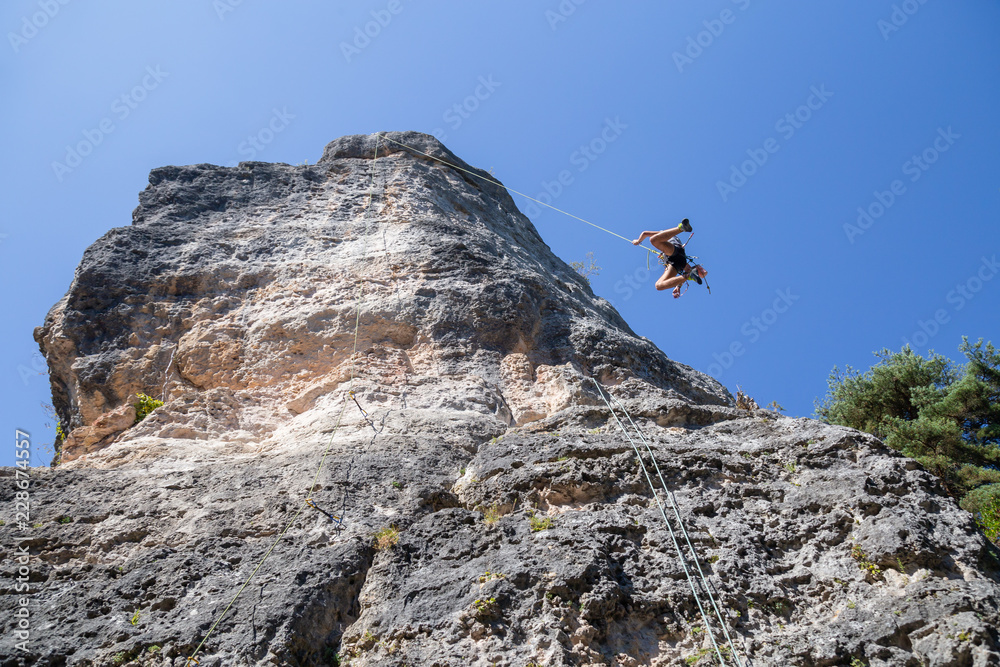 From below shot of climber secured with rope jumping from top of mountain under blue sky 
