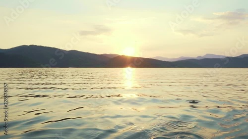 Slow motion happy young woman with her dog Jack Russell Terrier paddling on an inflatable kayak on the water of a large mountain lake against a beautiful orange sunset. Family Sports Weekend