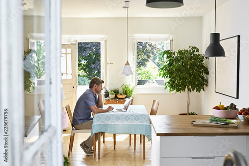 Mature man sitting in his dining room, using laptop