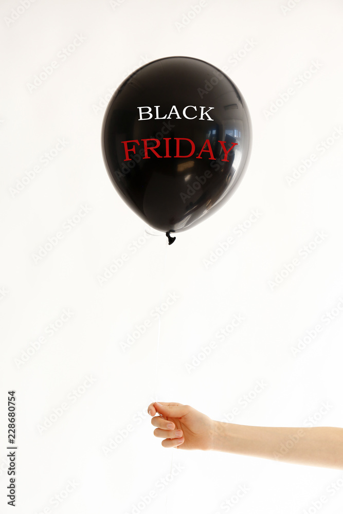 Obraz premium Black Friday on black balloon in girl's hand. Black friday sale concept. Fourth Friday of November, beginning of Christmas shopping season since 1952. Copy space, close up, top view, flat lay.