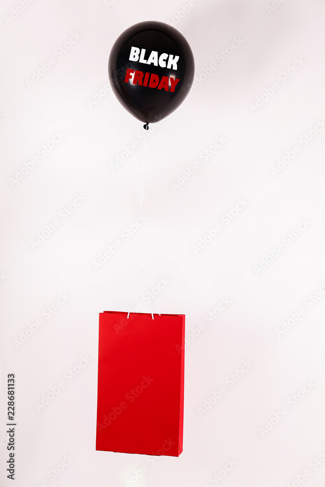 Obraz premium Black friday text on flying balloon lifting red shopping bag. Fourth Friday of November, beginning of Christmas shopping season since 1952. Copy space, close up, top view, flat lay, background.