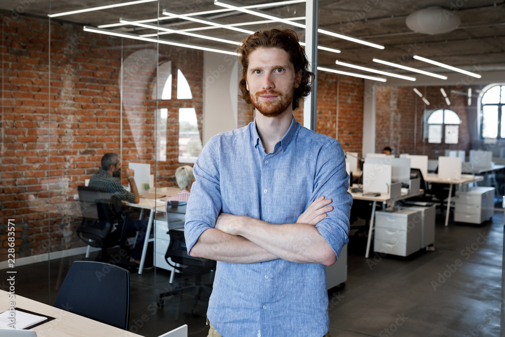 Portrait of young ginger businessman standing at office and looking at camera. Portrait of young ginger businessman standing at office and looking at camera.