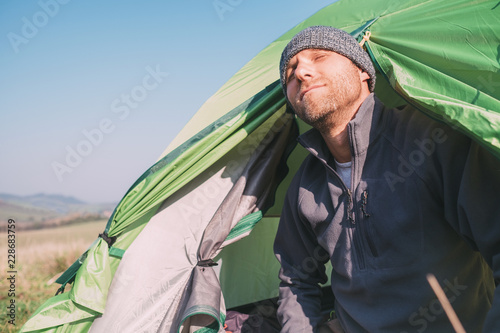 Breaded man traveler look out fronm tent and enjoy with sun light. Deep autumn or summer camping tourism photo