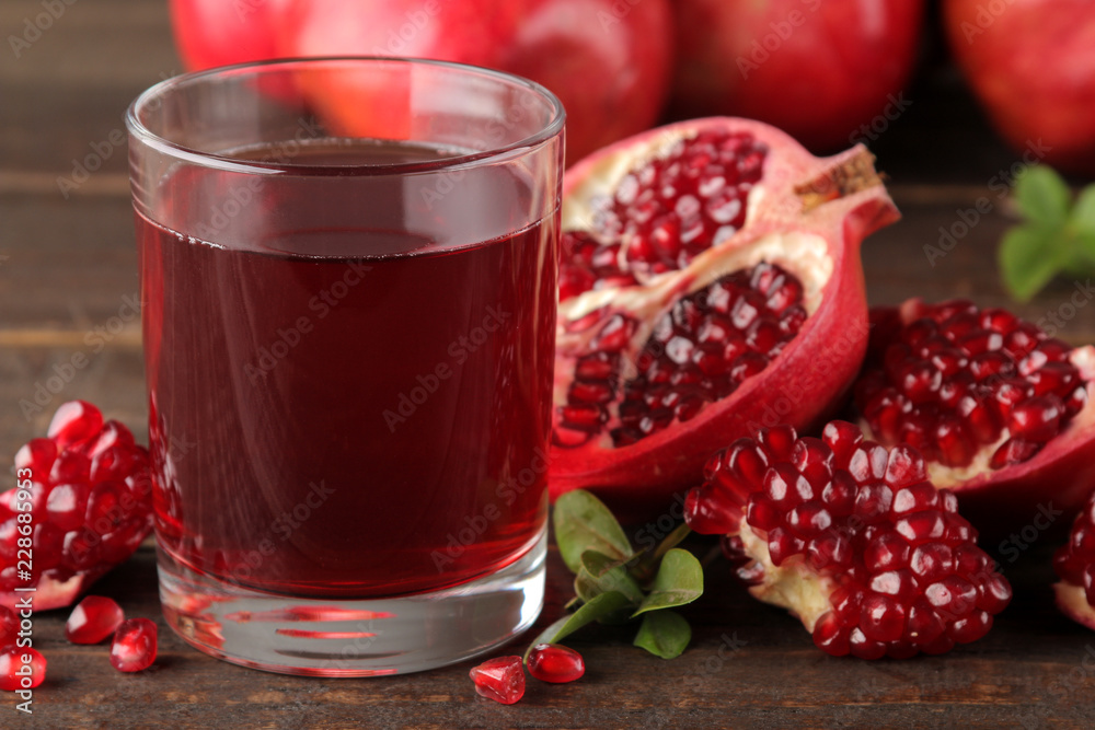 Pomegranate juice in a glass with fresh pomegranates around on a brown wooden table Pomegranate juice in a glass with fresh pomegranates around on a brown wooden table