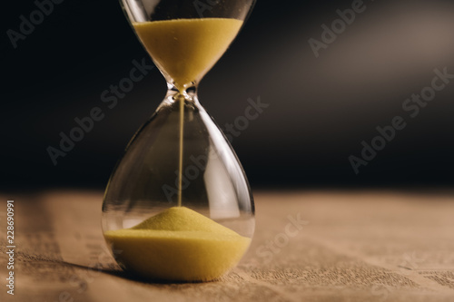 Hourglass with the sand running through on newspaper background with copy space, time passing concept for business deadline.