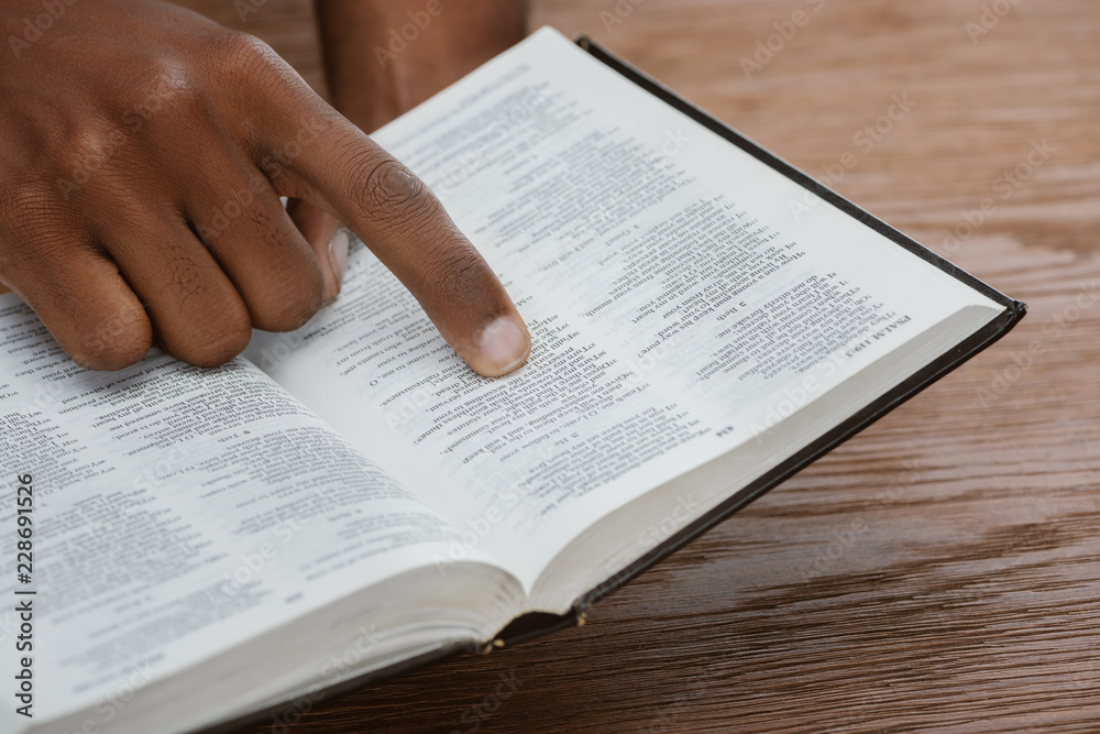 cropped shot of african american man reading holy bible and pointing at psalm cropped shot of african american man reading holy bible and pointing at psalm