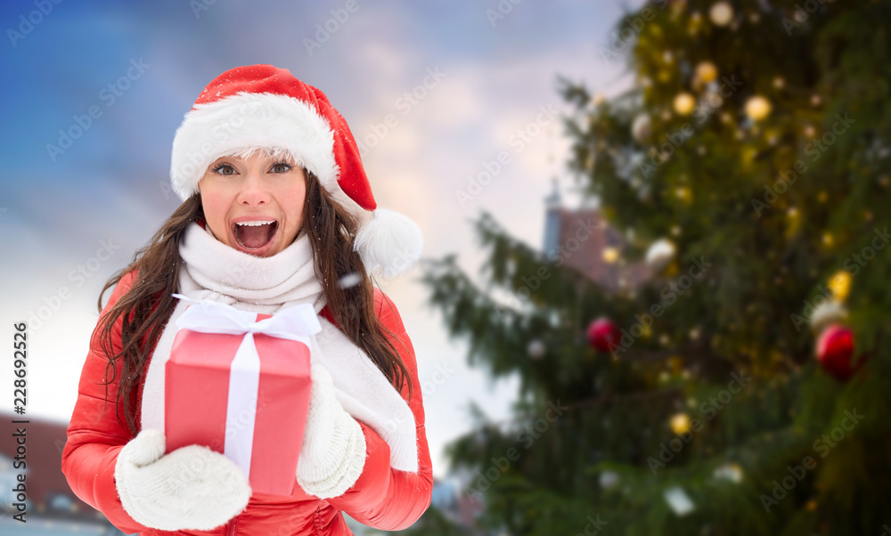 people, season and leisure concept - happy woman in santa hat with gift over christmas tree at tallinn old town hall square background people, season and leisure concept - happy woman in santa hat with gift over christmas tree at tallinn old town hall square background