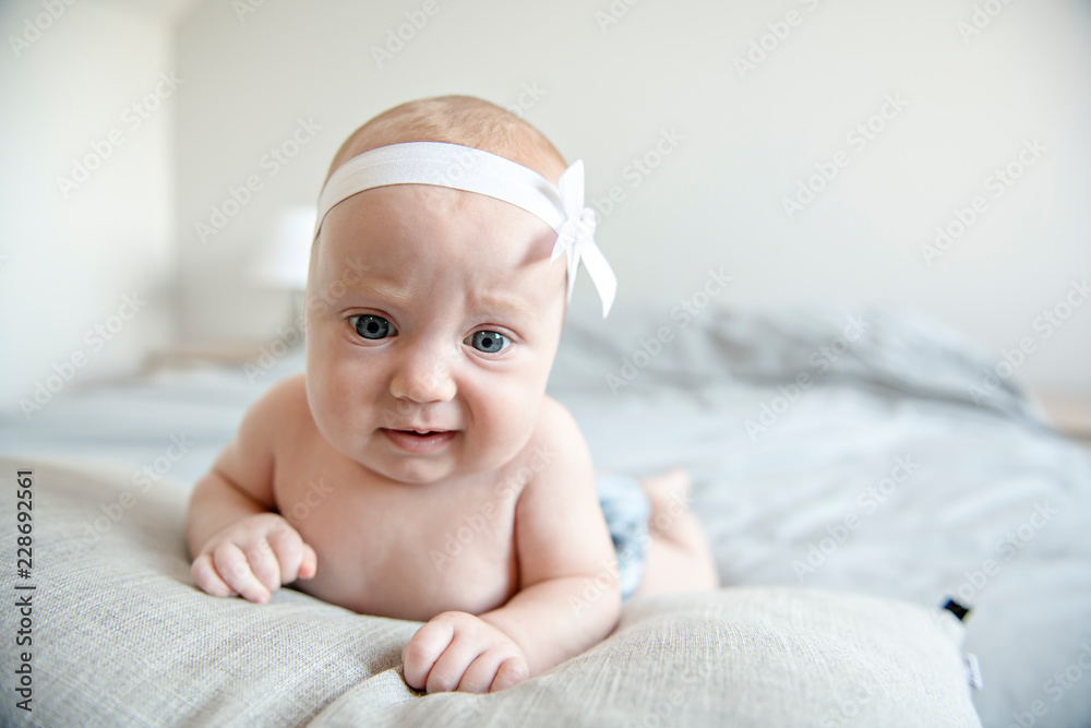 Adorable two months baby girl relaxing in bedroom on knitted blanket on a sunny morning