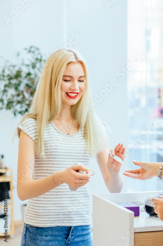 Young positive blond woman model paying with her credit card at the modern beauty shop interior. Payment process, servise and consumerism concept. Close up