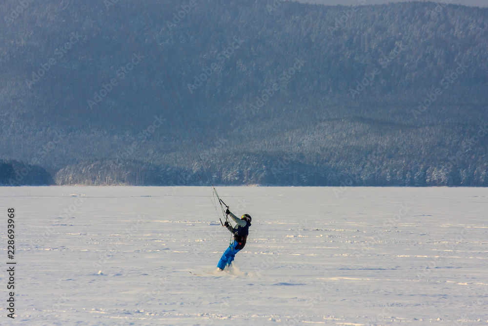snowkiting extreme winter sport. athletes on a wild winter mountain lake in the evening at sunset ride. fresh white snow and wind.