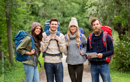 travel, tourism, hiking and people concept - happy friends or travelers with backpacks and map on road in woods