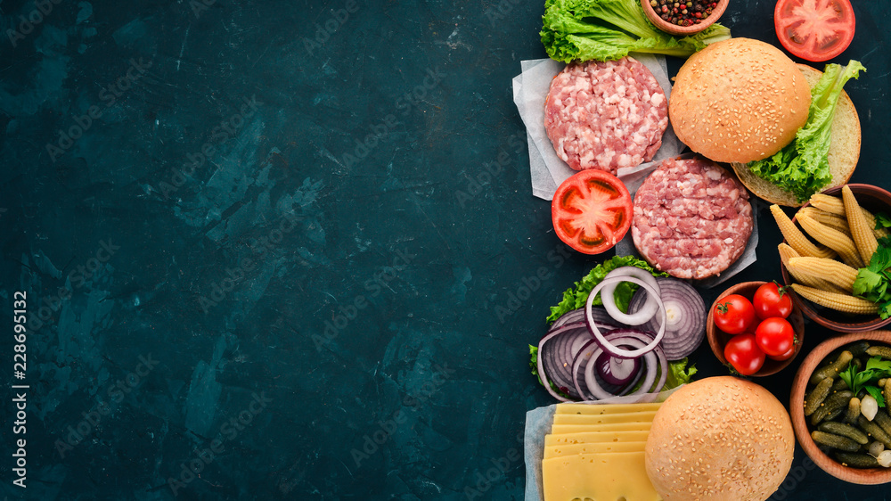 Preparation of burger. Meat, tomatoes, onions. On a black stone background. Top view. Free copy space.