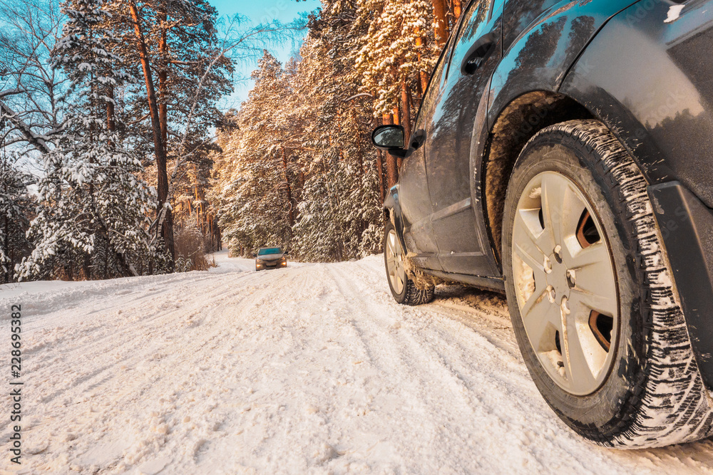 Luxury black crossover made a stop on the winter road in the forest. SUV. Car tires on winter road covered with snow. Vehicle on snowy alley in the morning at snowfall. Luxury black crossover made a stop on the winter road in the forest. SUV. Car tires on winter road covered with snow. Vehicle on snowy alley in the morning at snowfall.
