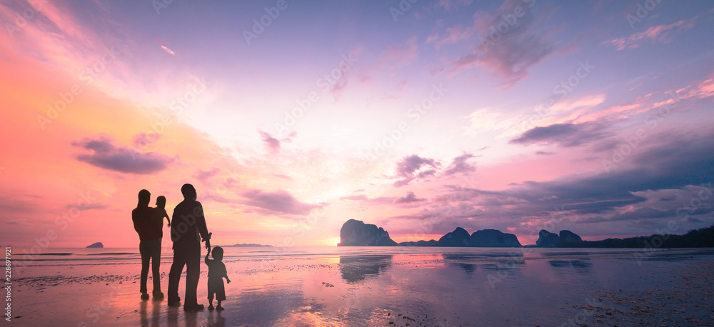 Fototapeta premium Silhouette of happy family with two children standing on the beach at sunset, purple and orange twilight sky over the ocean.