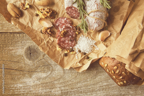 Italian salami wih sea salt, rosemary, garlic and nuts on paper. Rustic style. Top view.