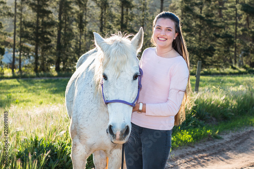 Teenage girl with a white Boerperd horse standing and looking at the camera smiling. photo