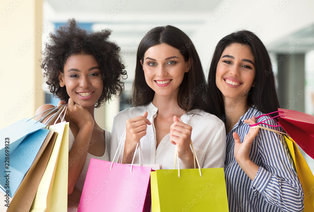 Three excited women with colourful bags shopping in mall Three excited women with colourful bags shopping in mall