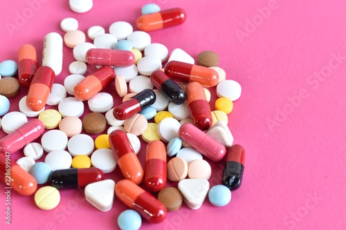 Multicolored isolated pills and capsules on the pink background