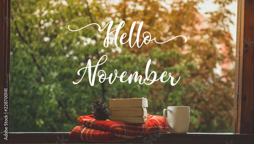 Hello November. Cozy autumn still life: cup and opened book on vintage windowsill with red blanket, pumpkin, candles. Autumn. Rain photo