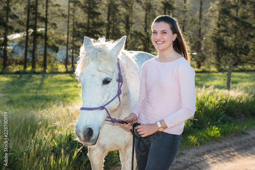 Teenage girl with a white Boerperd horse standing and looking at the camera smiling. photo