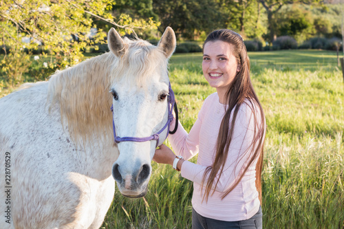 Teenage girl with a white Boerperd horse holding his head collar looking at the camera smiling. photo