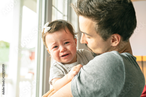 Father holding little girl close to the window, unhappy girl cry