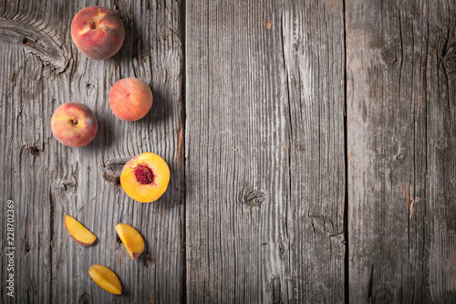 Flat lay view of whole and sliced peaches on weathered barn wood with generous copy space.