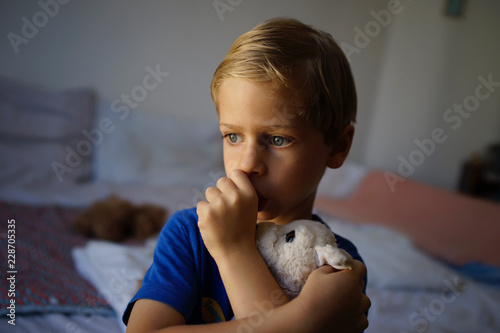 Canvas Print Vulnerable boy, insecure child, tired, holding soft toy, sucking thumb - at home