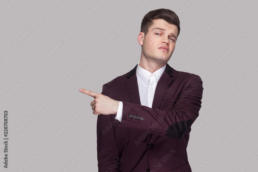 Get out. Portrait of serious handsome young man in violet suit and white shirt, standing, looking at camera with anger face and showing exit side. indoor studio shot, isolated on grey background. Get out. Portrait of serious handsome young man in violet suit and white shirt, standing, looking at camera with anger face and showing exit side. indoor studio shot, isolated on grey background.