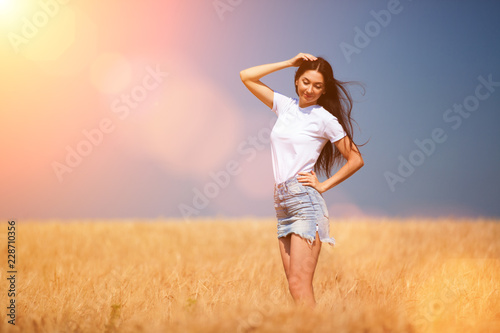 Happy fashion woman enjoying the life in the field. Nature beauty, blue sky and golden field with wheat. Outdoor lifestyle. Freedom concept. Woman in summer field of wheat